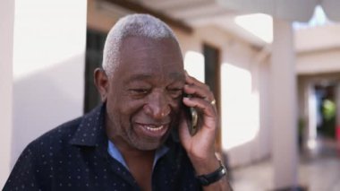 Dışarıda telefonla konuşan mutlu bir siyah Brezilyalı kıdemli adam. Dost canlısı karizmatik yaşlı kişi akıllı telefon cihazıyla modern teknolojiyi kullanarak sohbet ediyor.
