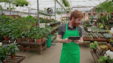 Mobil Erkek Çalışan Envanteri Çiçekçide Tablet ile kontrol ediyor. Yeşil Önlüklü Genç Adam Mağaza İşlemlerinde Modern Teknolojiyi Entegre Ediyor