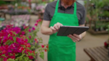Yerel işletmelerde çalışan kişilerin el ele tutuştukları tabletlerin envanterlerini tarıyoruz. Çiçekçi dükkanında modern teknoloji kullanan yeşil önlük giyen genç adam.
