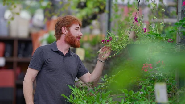 stock image Candid young redheaded man smelling flower at horticulture retail store