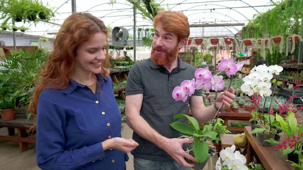 カメラを見ている間 工場内の花を保持幸せなカップルの肖像画笑顔 一緒に装飾のための赤毛の男と女性のショッピング — ストック写真