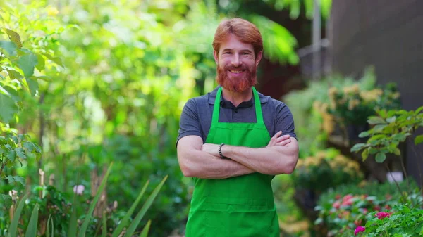 stock image One happy young male gardener wearing Green Apron with arms crossed smiling at camera in natural garden environment