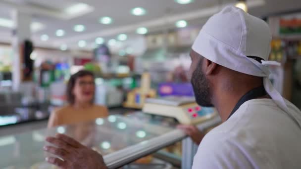 お客さんと話すカフェテリアカウンターの後ろの従業員 フードサービス店の女性を助ける帽子の髪を身に着けている黒いスタッフ — ストック動画