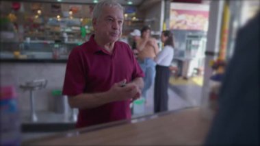 Kafeteryanın kasiyerlik bölümündeki kıdemli müşteri cep telefonu ödemesiyle ödeme yapıyor. Yaşlı kişi ulaşılamayan telefonla ödeme yapıyor.