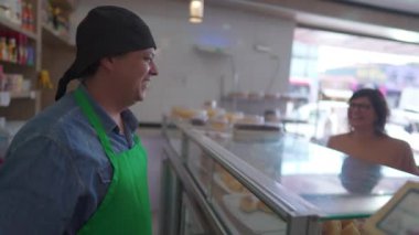 Şarküteri tezgahının arkasındaki mutlu çalışan kafeteryadaki müşterilerle iletişim kuruyor. Kadınlar restoranda yemek siparişi veriyor.