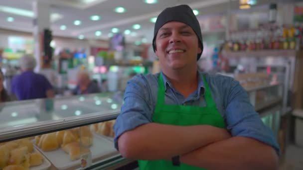 レストランのカフェテリアでデリカウンターの後ろに腕を交差中小企業の幸せな男性従業員 ブラジル系南米人スタッフ — ストック動画
