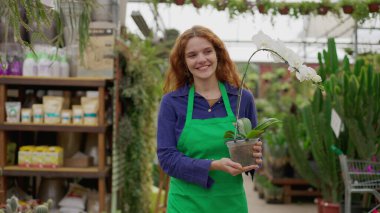 Bahçecide çiçek taşıyan mutlu kadın çiçekçi. Genç, kızıl saçlı, yeşil önlüklü bir kadın yerel bir dükkanda çalışıyor.