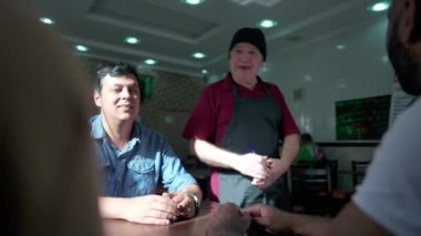 İnsanlar restoranda yemek sipariş ediyor, erkek garson geleneksel Brezilya kafeteryasında oturan müşterilerden emir alıyor.