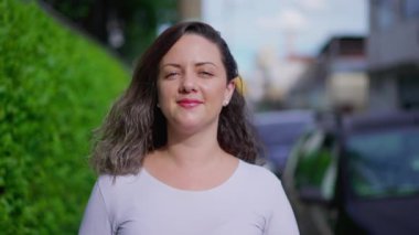 30 'lu yaşlarındaki neşeli genç kadın ağır çekimde gülümseyerek kaldırımda yürüyor.
