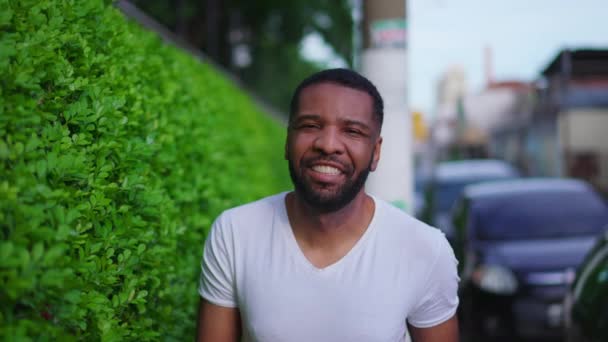 一个快乐的巴西黑人男人走在街上的人行道上 对着摄像机笑着 友好的人 在运动中的近距离跟踪镜头 — 图库视频影像