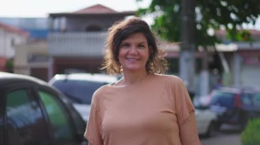 50 'li yaşlarda mutlu bir kadın kaldırımda kameraya gülümsüyor. Brezilyalı orta yaşlı bir kadının portresi yakın çekim hareketini yakından takip ediyor.