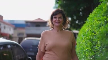 Kendine güvenen bir ifadeyle kaldırımda yürüyen neşeli olgun bir kadın. Orta yaşlı bir Brezilyalı ileri doğru yürür