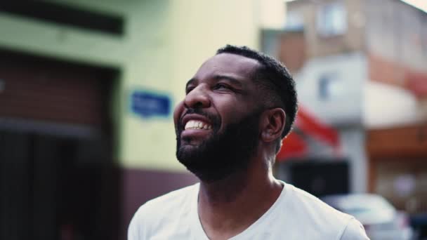 都会の外に立つアフリカ系アメリカ人の楽しい男が 希望に満ちた瞑想的な表情で笑って空を見上げている — ストック動画