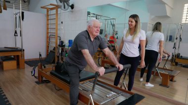 Omurga Çalışması Rutinindeki Yaşlı Adam, Pilates Stüdyosu Eğitmeni: Kadın Eğitmen