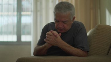 Sadık kıdemli adam evde haç işareti yapıyor, Kafkasyalı yaşlı erkek koltukta dua ediyor, ruhaniliği ve umudu somutlaştırıyor