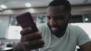 Elinde cep telefonu cihazı olan mutlu siyah Brezilyalı bir adam gülümsüyor. Afrikalı Amerikalı telefon ekranına bakıyor.