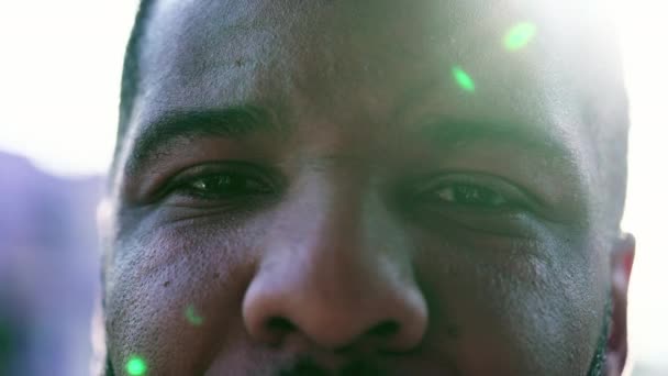 太陽の光のフレアが輝くカメラを見ている1人の黒い男のクローズアップ目 アフリカ系アメリカ人の中立的な表情 強烈な視線 — ストック動画
