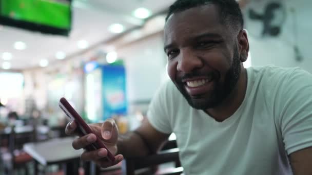 一个快乐的巴西黑人男子手持电话 微笑着看着传统自助餐厅里的相机的画像 — 图库视频影像