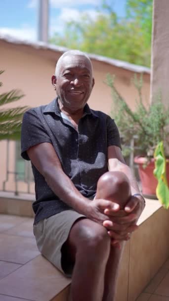 一位快乐的巴西黑人老人坐在自家后院的垂直录像中对着摄像机微笑 — 图库视频影像