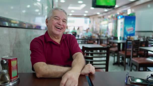 Один Щасливий Старший Чоловік Сміється Посміхається Сидячи Всередині Південноамериканської Кафетерії — стокове відео