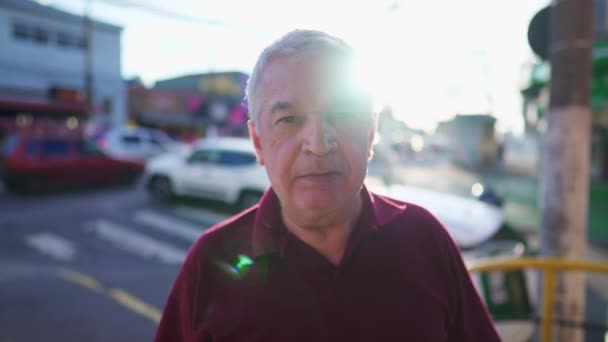 日光がバックライトに輝く都会の環境に立つ先輩の肖像画 70代の高齢者が市内に立つ — ストック動画