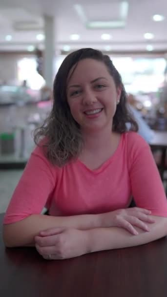 一个快乐的年轻女人坐在餐厅餐厅里对着相机微笑的画像 一个30多岁的女性在垂直视频中 — 图库视频影像