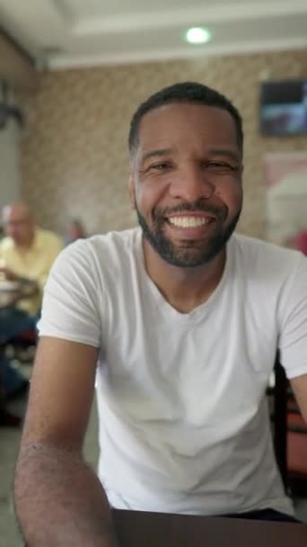 Один Счастливый Бразильский Черный Мужчина Улыбается Камеру Сидя Кафетерии Ресторана — стоковое видео