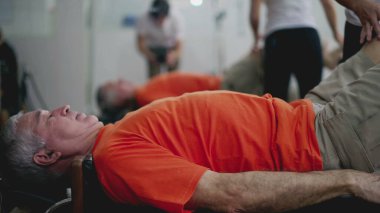 Fizyoterapist yaşlı adamın pilates makinesini kullanmasına yardım ediyor. Yaşlılık rutini, vücut sağlığı ve dayanıklılık.