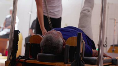 Kadın eğitmen tarafından çalıştırılan pilates makinesini kullanan kişi. Kıdemli bir siyahi kadın egzersiz yaparak sağlığına dikkat ediyor.