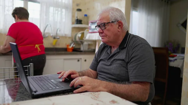 老男人在笔记本电脑前使用现代技术在家庭厨房设置 在家里与计算机打交道的高年级男生 — 图库照片