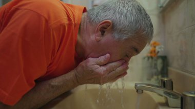 Yaşlı adam sabah rutin yaşam tarzında banyo lavabosu ile yüzünü yıkıyor.