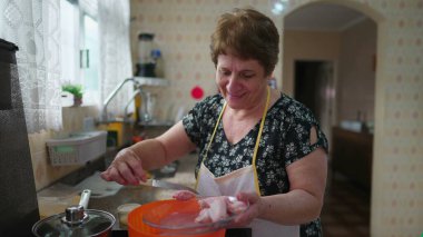 Mutfakta ayakta yemek pişiren mutlu yaşlı kadın. Neşeli yaşlı bayan evde öğle yemeği hazırlıyor, gerçek hayat ev hayatı tarzı.