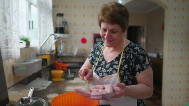 Mutfakta ayakta yemek pişiren mutlu yaşlı kadın. Neşeli yaşlı bayan evde öğle yemeği hazırlıyor, gerçek hayat ev hayatı tarzı.