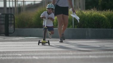 Aktif çocuk yaya geçidinde üç tekerlekli scooterla karşıdan karşıya geçiyor. Küçük bir çocuk oyuncak taşımacılığıyla dışarıda egzersiz yapıyor.