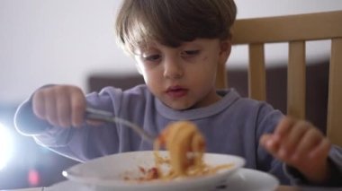 Çocuk makarna yiyor. Küçük çocuk tek başına spagetti yiyor.