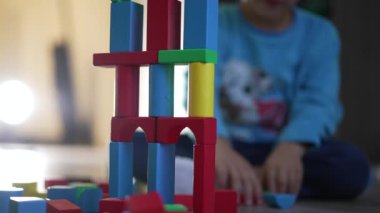 Çocuk renkli oyuncak blokları yapmakla oynuyor. Küçük bir çocuk, yatak odasında yerde duran bloklardan bir kule inşa ediyor.