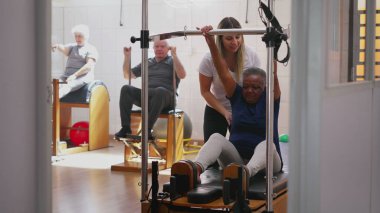 Kadın pilates koçu grup sınıfında siyahi bir kadına yardım ediyor. Sağlık hizmetleri spor eğitmeninin gizli bir sahnesi.