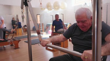 Pilates Stüdyosu Grup Toplantısı 'nda egzersiz yapan yaşlı kişi. Yaşlı bir beyaz adam makineyle vücuduna bakıyor.