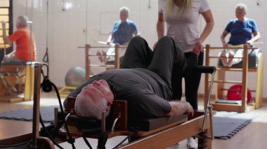 Pilates koçu, beden ve bacakları güçlendirmek için makineyi kullanmasına yardım ediyor. Omurga sağlığı ve esneklik yaşlılık egzersizleri rutin yaşam tarzı