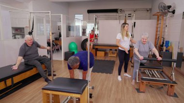 Pilates Grup Yaşlılar Egzersizi Eğitmen koçunun yardımıyla makineleri kullanmaları için onları yönlendirerek