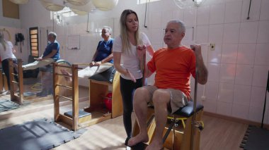 Pilates Makinesi 'nin kadın eğitmen tarafından çalıştırıldığı son sınıf egzersiziniz kutlu olsun. Yaşlılıkta vücut sağlığıyla ilgilenen yaşlı kişi rutin egzersiz yapar.