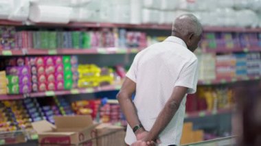 Üst düzey bir müşterinin marketteki ürünlere göz atması, raftan alınacak eşyalara bakması. Samimi ve tüketici yaşam tarzında yaşlı bir müşteri.
