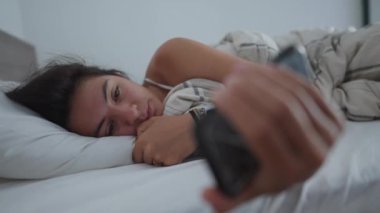Sabah yatağında telefon ekranına bakan bir kadın. Üzgün bir kadın, elinde akıllı telefonuyla yataktan kalkıp mesaj okuyamıyor.