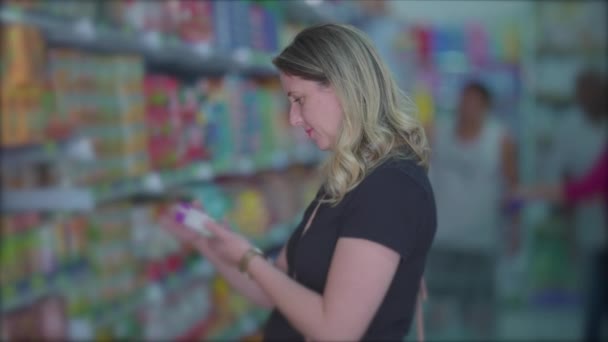通路の内側の棚からアイテムを見て女性の食料品店 女性は製品ラベルを読む — ストック動画