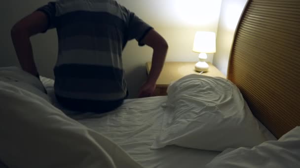 男は長い一日の後に休むためにベッドに横たわっていた ベッドシートの下で寝る人はベッドサイドランプをオフにして休憩 — ストック動画