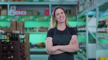 Süpermarketin mutlu kadın çalışanı kollarını kavuşturmuş, markette önlük giymiş bir kadının neşeli ifadesi.