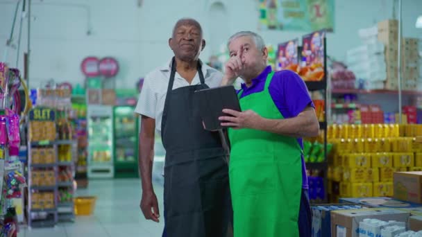 两名在超市工作的高级员工正在查看平板电脑设备 杂货店为员工提供指导的老经理团队合作场景 职业理念 — 图库视频影像