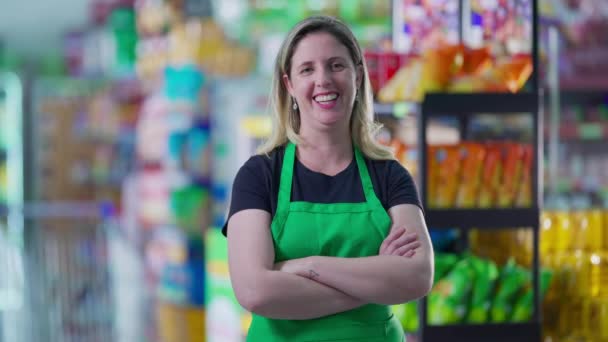 スーパーマーケットの通路の中に立ちカメラを眺めながら腕を組んで笑顔で笑っている楽しそうな女性社員の姿が描かれています 職業概念は — ストック動画