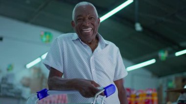 Brezilyalı son sınıf müşterisi süpermarketin içinde alışveriş arabasıyla kameraya gülümsüyor. Marketteki Afrikalı Amerikalı yaşlı tüketicinin portresi