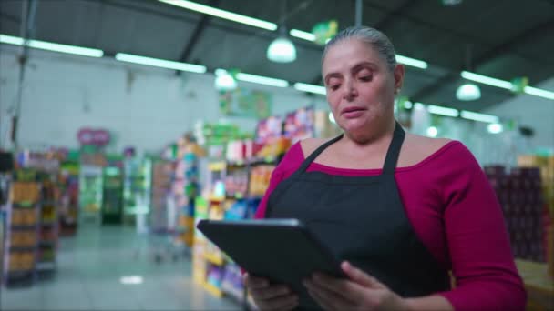 テーブルデバイスの画面を見ながら職場での不満や不安を感じながらビジネスの中に立つスーパーマーケットチェーンのストレス女性社員 — ストック動画